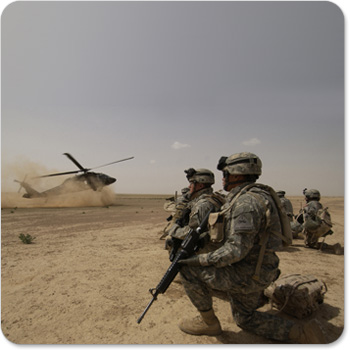 Several soldiers in the sandy desert watch a helicopter land close by.