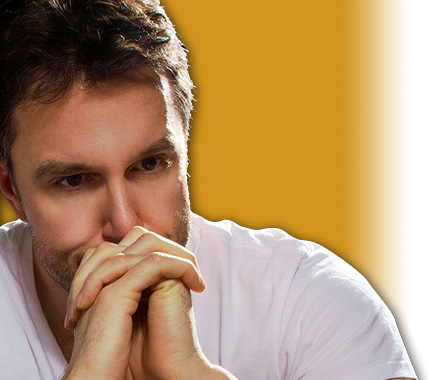 man sitting with hands clasped in front of his mouth.