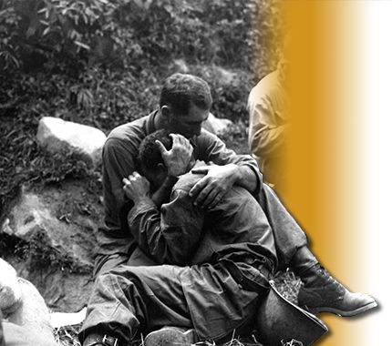 Soldiers holding each other on the battlefield.