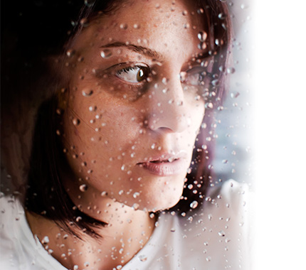Woman looking out of a window afraid.