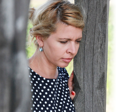 a young woman looking pensive leaning on a wooden post 